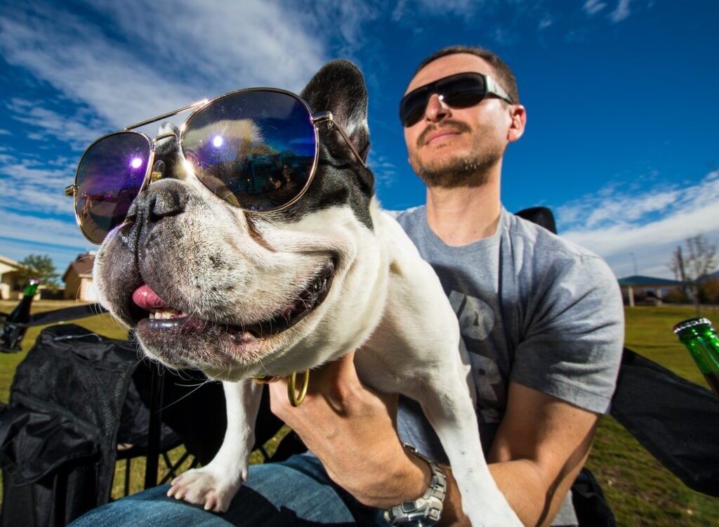 man in black sunglasses holding white short coated dog