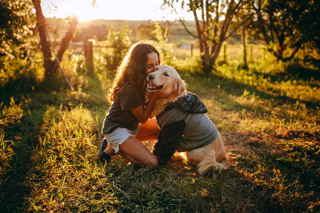- NeposlušnéTlapky woman in black t-shirt and brown shorts sitting on brown grass field with white dog