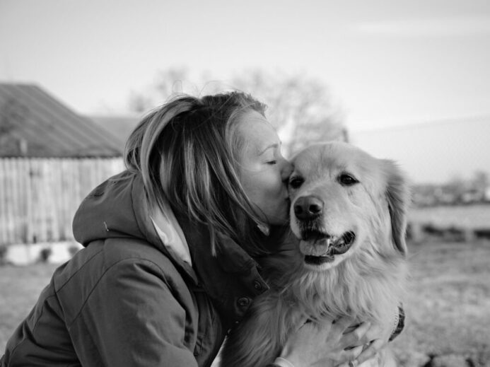 grayscale photo of woman kissing golden retriever