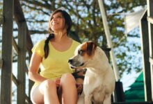 woman in yellow shirt sitting beside white and brown short coated dog