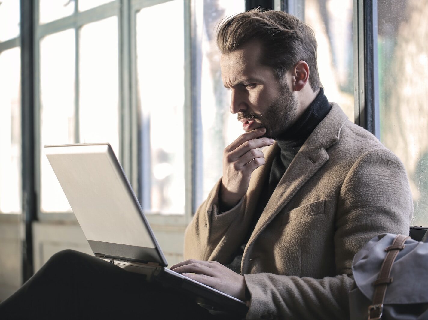 man holding his chin facing laptop computer