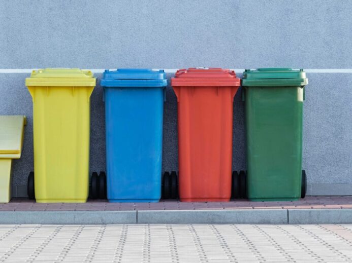 four assorted-color trash bins beside gray wall