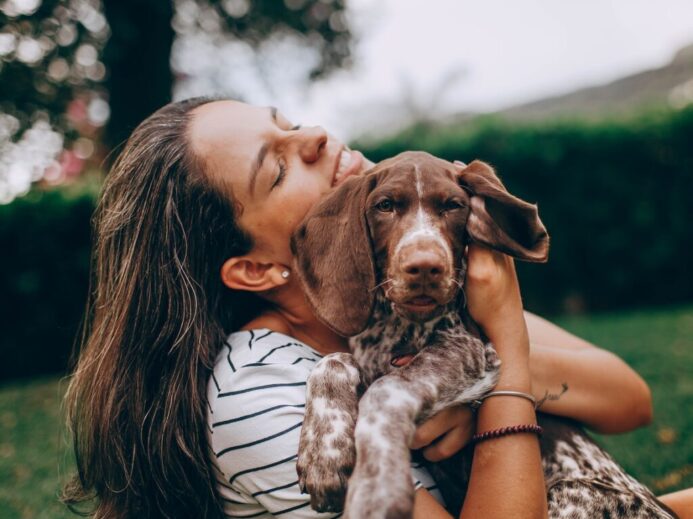 woman in white and black stripe tank top hugging brown and white short coated dog
