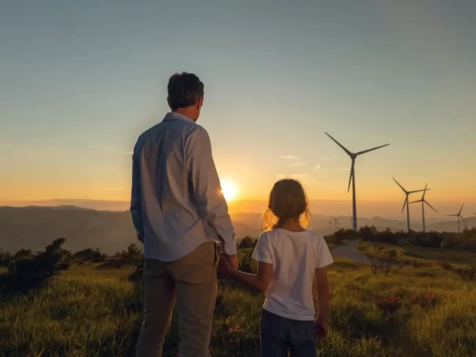 Muž s chlapcem se dívají na větrné elektrárny v západu slunce